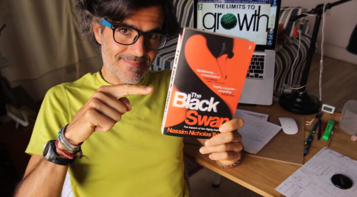 Angel Abril Ruiz con el libro «The Black Swan» en la mano y la imagen del libro «The Limits To Growth» en el ordenador de fondo
